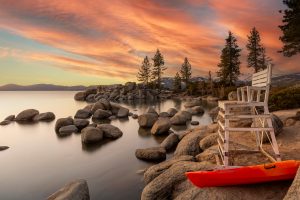 Beautiful sunset view over Lake Tahoe with rocks, trees, and a chair adding to the tranquil scene.
